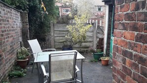 A small outdoor patio area with a metal table and chairs, surrounded by brick walls and potted plants. - Grand 4-Bed Quasi semi House in Manchester (Manchester)