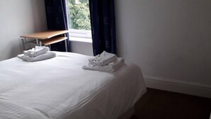 A neatly made bed with white linens and towels, a wooden nightstand, and a window with curtains. - Grand 4-Bed Quasi semi House in Manchester (Manchester)