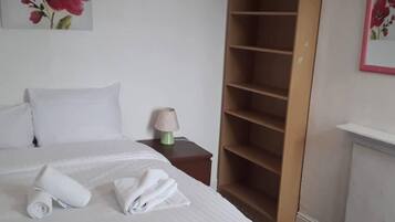 A neatly made bed with a folded towel, a bedside lamp, and a wooden wardrobe with multiple shelves.