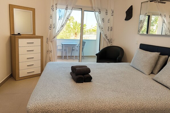A bedroom with a bed, a dresser, a chair, and a balcony with a table and chairs. - Lagos Marina view apt  on main avenue near beaches (Lagos)