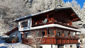 A two-story chalet with a balcony, surrounded by snow-covered trees. - Apartment "Petra" with Mountain View, Balcony & Wi-Fi (Kössen)