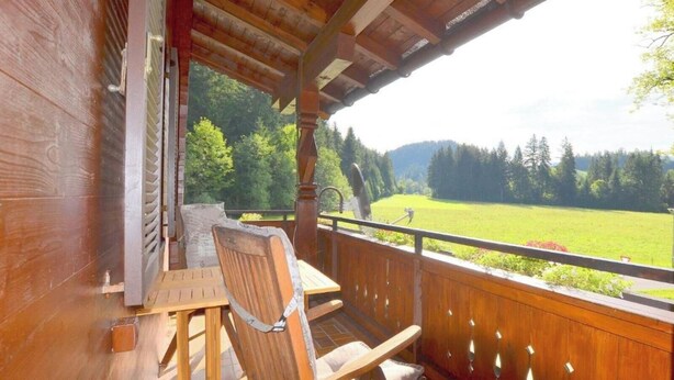 A wooden deck with a table and chairs, overlooking a green landscape with trees and a field. - Apartment "Petra" with Mountain View, Balcony & Wi-Fi (Kössen)