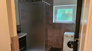 A compact bathroom with a shower, a washing machine, and a window. - Apartment "Petra" with Mountain View, Balcony & Wi-Fi (Kössen)
