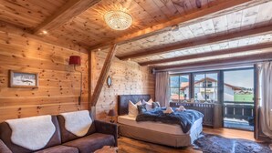 A log cabin bedroom with a bed, a sofa, a chandelier, and a view of the outside. - Chalet "Alpine Time-Out in Swiss Pine Wood" with Mountain View in Inzell near Ruhpolding (Inzell)