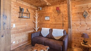 A wooden cabin interior with a brown sofa, a wooden floor, a lamp, and a wall-mounted shelf. - Chalet "Alpine Time-Out in Swiss Pine Wood" with Mountain View in Inzell near Ruhpolding (Inzell)