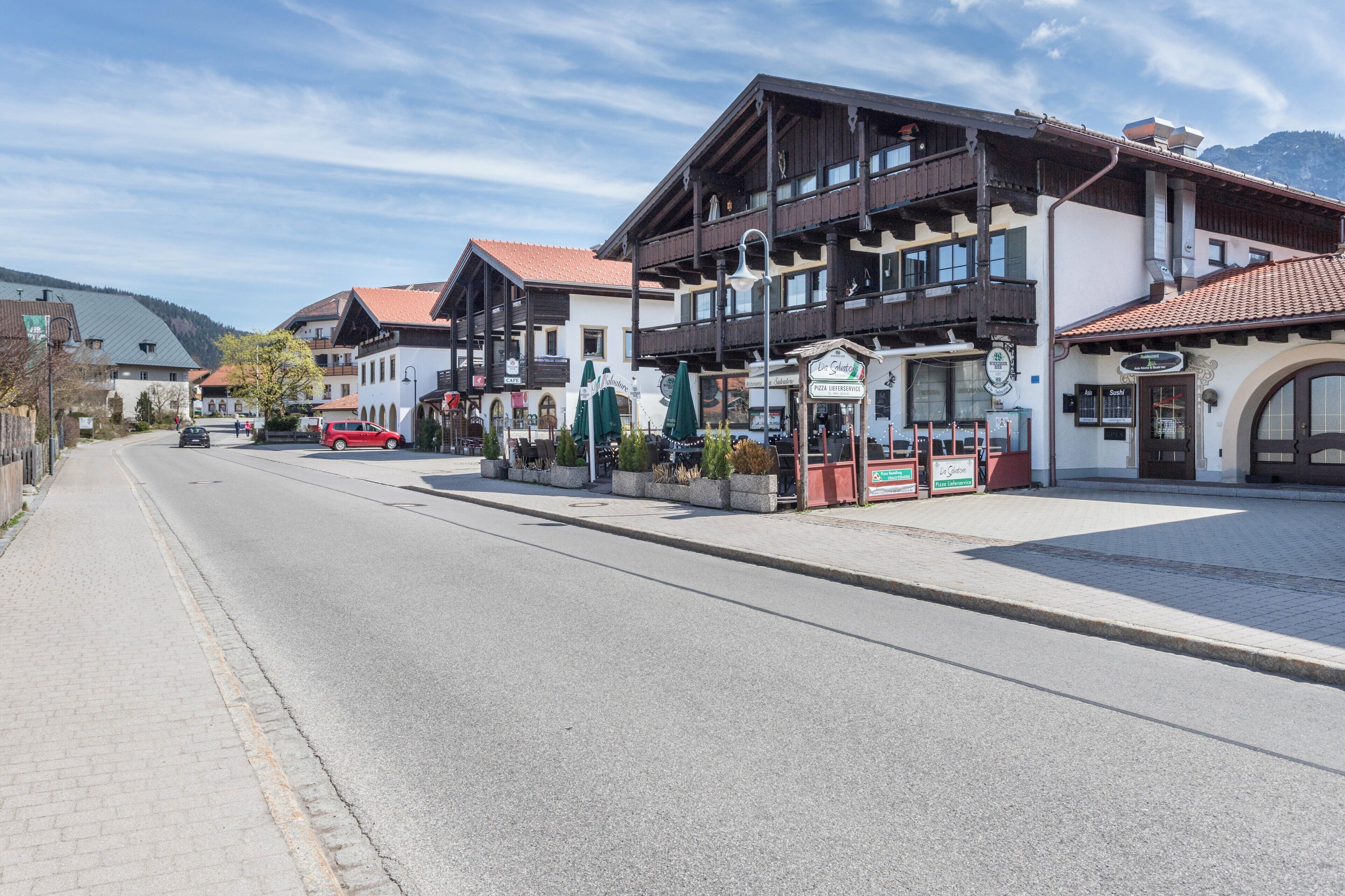 A street with buildings, including a restaurant with outdoor seating and a sign.