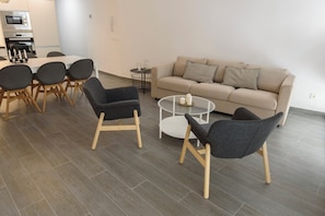 A modern living room with a sofa, two armchairs, a coffee table, and a dining area with chairs and a table.