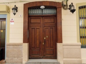 A wooden double door with a small window above it, a sign indicating a direct alarm with police, and a number '5' on the wall to the left. - RENTHAS Fernando Lessesps I (Malaga)