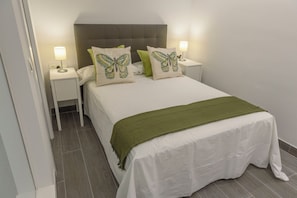 A neatly made bed with a green throw blanket, two bedside lamps, and butterfly-themed pillows.