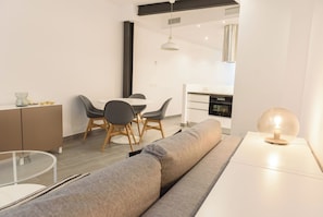 A modern living room with a sofa, a glass coffee table, and a dining area with a round table and chairs.