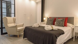 Ein modernes Hotelzimmer mit Bett, Sessel, Kleiderschrank und Nachttisch.
