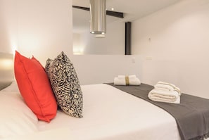 A neatly made bed with a red pillow, a patterned pillow, and a folded towel on a dark-colored bedspread.