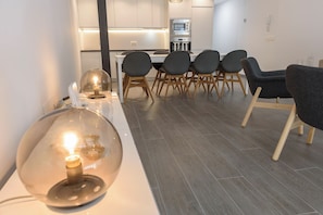 Ein moderner Essbereich mit einem weißen Tisch, grauen Stühlen und einer großen Glasleuchte.