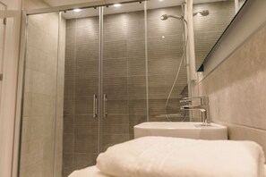 Een moderne badkamer met een glazen douchecabine, een witte wastafel en een handdoek op het aanrecht.