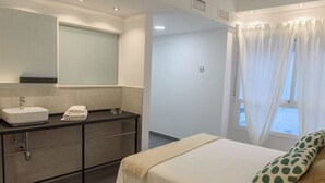 Ein Schlafzimmer mit Bett, ein Badezimmer mit Waschbecken und Spiegel sowie ein Fenster mit Vorhängen.