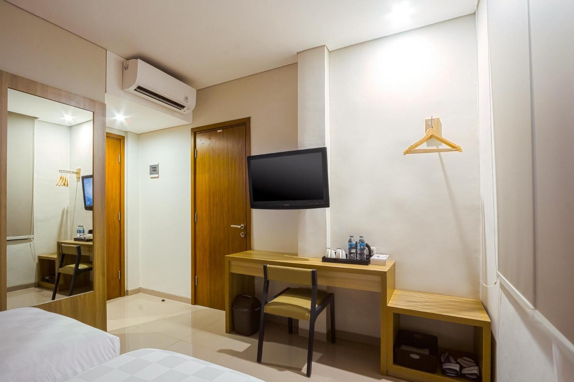 Una habitación de hotel con cama, escritorio y silla, televisor y perchero.