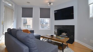 A modern living room with a grey sofa, a wooden coffee table, and a fireplace. - Chic 2-Bedroom Townhouse with Rooftop, Free Parking, in Downtown Chicago! (Chicago)