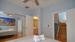 A bedroom with a bed, a ceiling fan, a cityscape painting, a bathroom with a mirror and sink, and a wooden staircase. - Chic 2-Bedroom Townhouse with Rooftop, Free Parking, in Downtown Chicago! (Chicago)