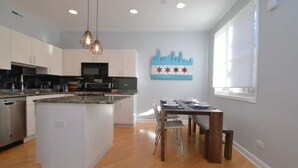A modern kitchen with white cabinets, a central island, and a dining area with a wooden table and chairs. - Chic 2-Bedroom Townhouse with Rooftop, Free Parking, in Downtown Chicago! (Chicago)