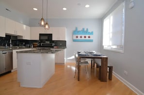 A modern kitchen with white cabinets, a central island, and a dining area with a wooden table and chairs. - Chic 2-Bedroom Townhouse with Rooftop, Free Parking, in Downtown Chicago! (Chicago)