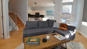 A modern living room with a grey sectional sofa, a wooden coffee table with books and candles, and a staircase leading to an upper floor. - Chic 2-Bedroom Townhouse with Rooftop, Free Parking, in Downtown Chicago! (Chicago)
