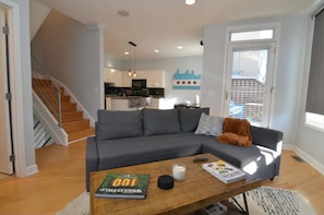 A modern living room with a grey sectional sofa, a wooden coffee table with books and candles, and a staircase leading to an upper floor. - Chic 2-Bedroom Townhouse with Rooftop, Free Parking, in Downtown Chicago! (Chicago)