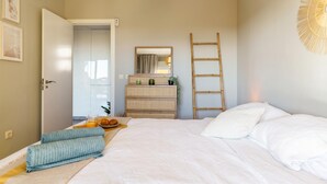 A bedroom with a bed, a bedside table with a lamp, a mirror, a dresser, and a wall-mounted ladder. - Calahonda Royale Seaview Suite, Mijas Costa, Spain (Mijas Costa)