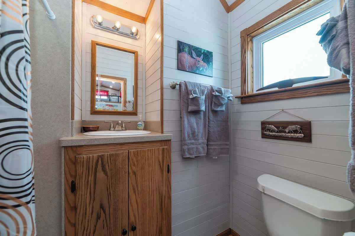 A bathroom with a wooden vanity, a mirror, a sink, and a window.