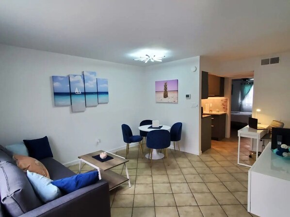 A modern living room with a sofa, a dining table with chairs, and artwork on the walls.