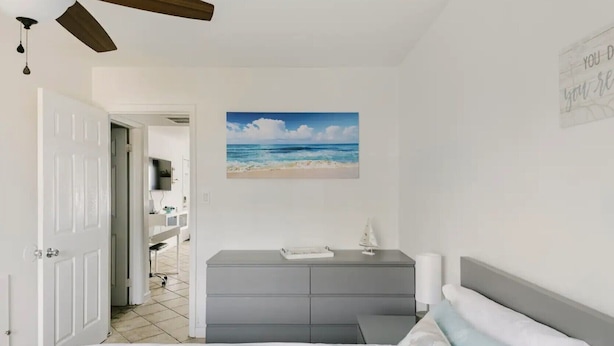 Ein Schlafzimmer mit einem Bett, einem Schminktisch, einem Strandbild und einem Deckenventilator.