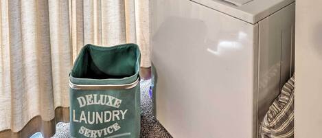 A front-loading white washer and dryer unit with a green laundry basket labeled "Deluxe Laundry Service" beside it.