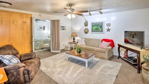 A living room with a brown leather sofa, a beige sofa, a wooden coffee table, a ceiling fan, a television, and a sliding door leading to a bedroom. - Akron Apartment w/ Balcony - Hunting Nearby! (Akron)