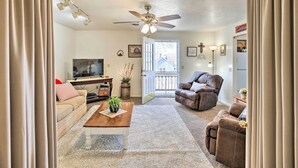 A living room with a ceiling fan, a television, a brown leather chair, a beige sofa, and a wooden coffee table. - Akron Apartment w/ Balcony - Hunting Nearby! (Akron)