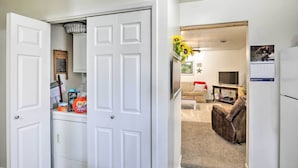 A compact living space with a white door, a laundry area, a sofa, and a TV in the background. - Akron Apartment w/ Balcony - Hunting Nearby! (Akron)