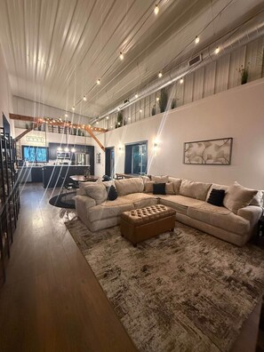 A spacious living area with a large sectional sofa, a wooden coffee table, and a staircase leading to an upper level. - Feathered Nest at Fellows Lake w/ Indoor POOL! (Fair Grove)