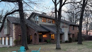 A two-story brick house with a stone chimney, a covered porch, and a lawn with outdoor furniture.