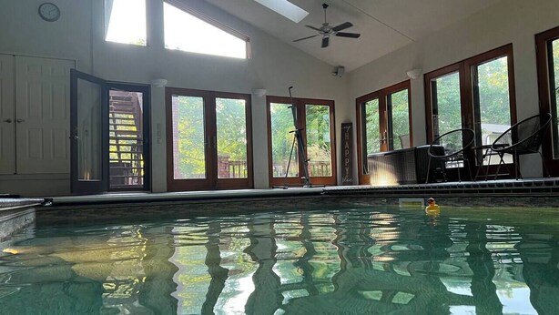 An indoor swimming pool with clear water, large windows, and ceiling fans.