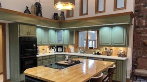 A kitchen with green cabinets, a wooden island, and a brick wall.