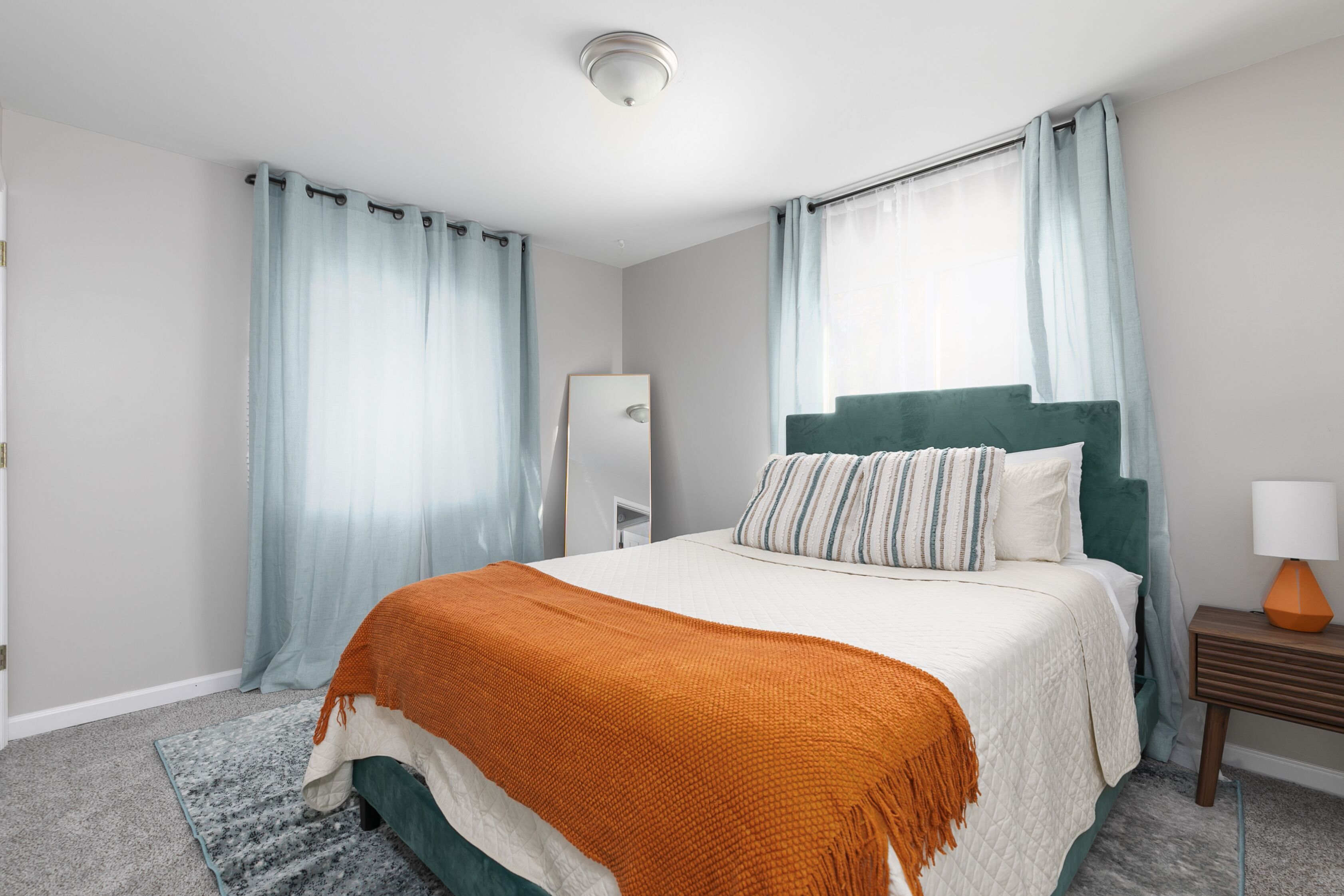 Une chambre à coucher moderne avec un lit, des rideaux, une table de chevet avec une lampe et un luminaire fixé au mur.