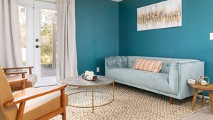 Een woonkamer met blauwgroene wanden, een lichtblauwe bank, een rond salontafeltje en een houten stoel.
