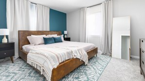 Een moderne slaapkamer met een houten bed, witte beddengoed en een wand in teal.