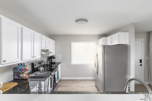 A modern kitchen with white cabinets, a stainless steel refrigerator, and a window with blinds.