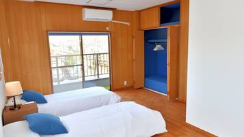 A room with two beds, a window with a view, a wardrobe, and a ceiling fan.
