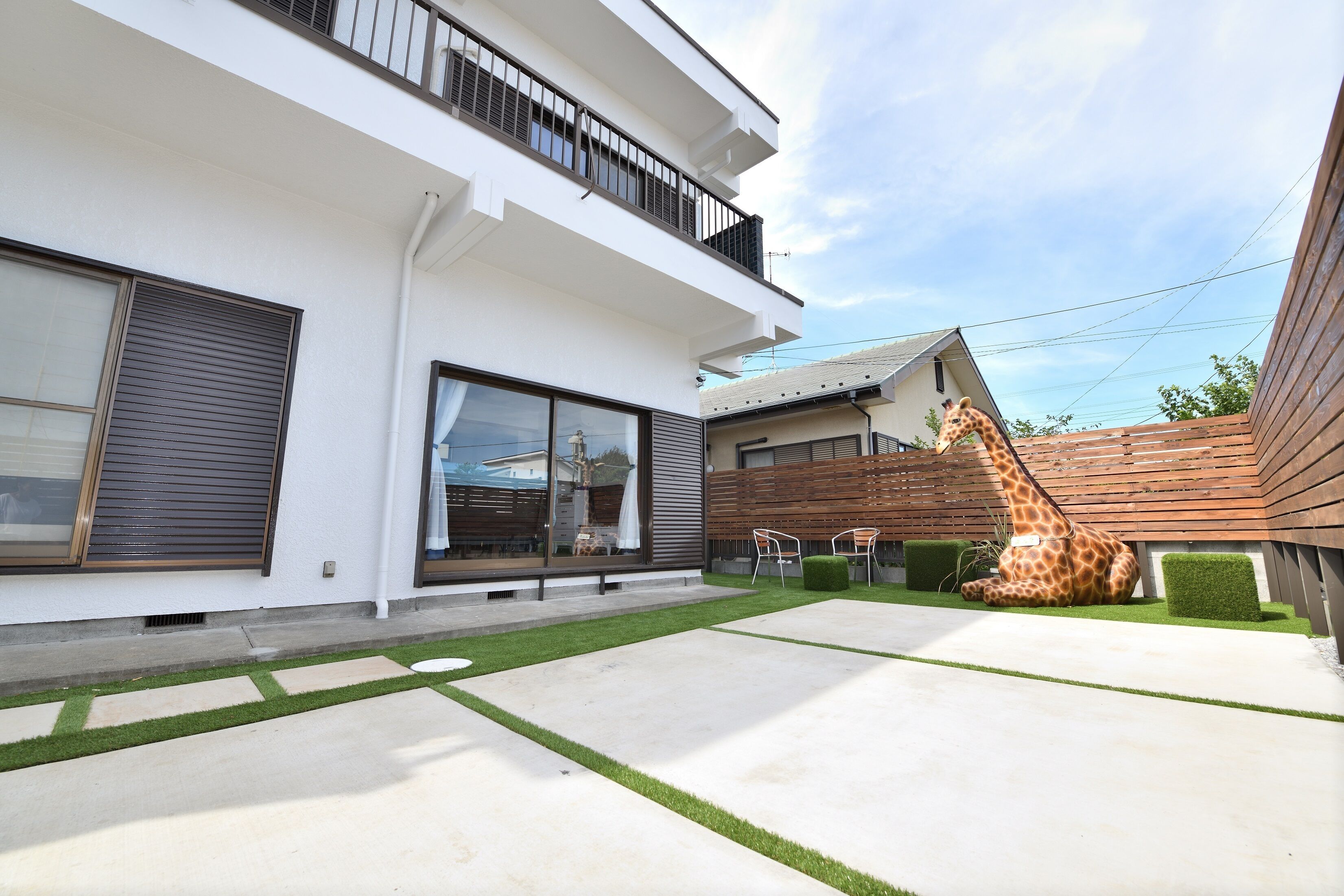 A modern two-story house with a large front yard, a wooden fence, and a giraffe statue.