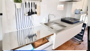 Une cuisine moderne dotée d’un évier en acier inoxydable, d’un plan de travail intégrant une balance et d’une étagère suspendue au-dessus de l’évier pour ranger les casseroles.