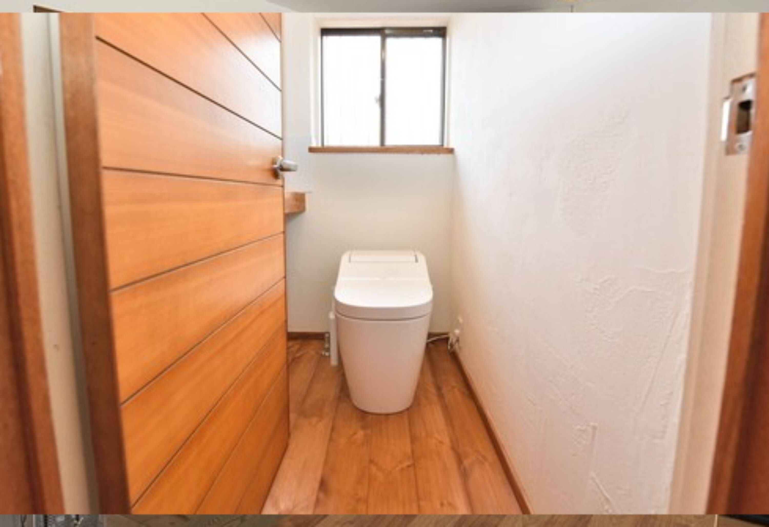 A narrow hallway with wooden flooring and a white toilet.