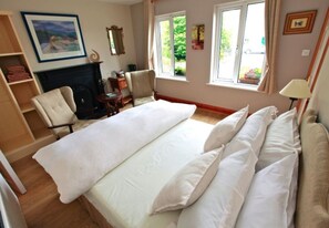 A bedroom with a large bed, a fireplace, a chair, and a window with a view of greenery. - Fough East, Oughterard (Oughterard)