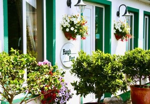 A building facade with a sign reading 'Bough East,' green window frames, and flower baskets on the wall. - Fough East, Oughterard (Oughterard)