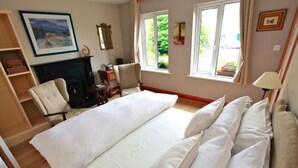A bedroom with a large bed, a chair, a fireplace, and a window with a view of greenery. - Fough East, Cozy and close to town (Oughterard)
