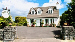 A two-story house with a tiled roof, a front porch with potted plants, and a sign that reads "Fough East." - Fough East, Cozy and close to town (Oughterard)